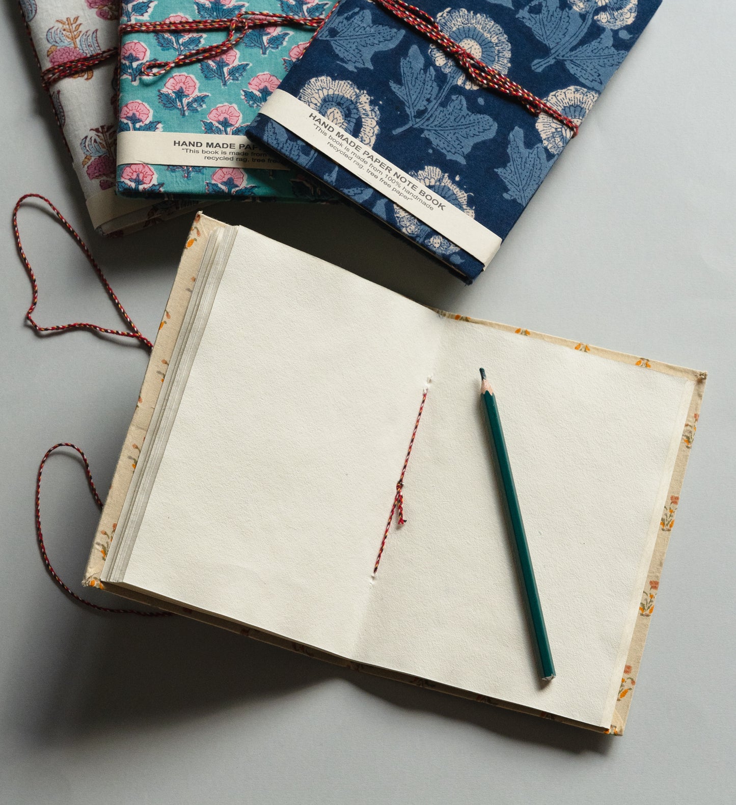 Open notebook with a pen on a gray surface, surrounded by patterned notebooks.