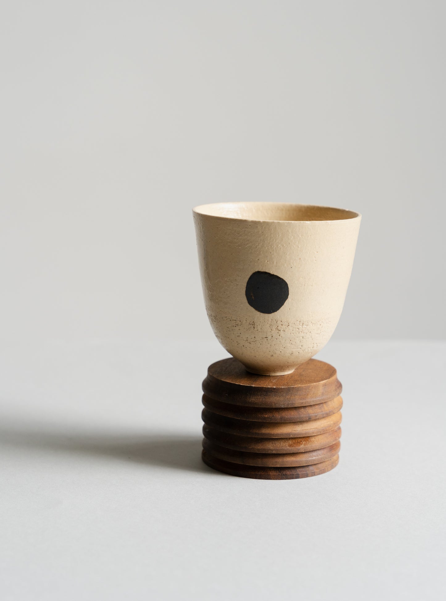 Ceramic cup with a black dot on a wooden stand against a light gray background