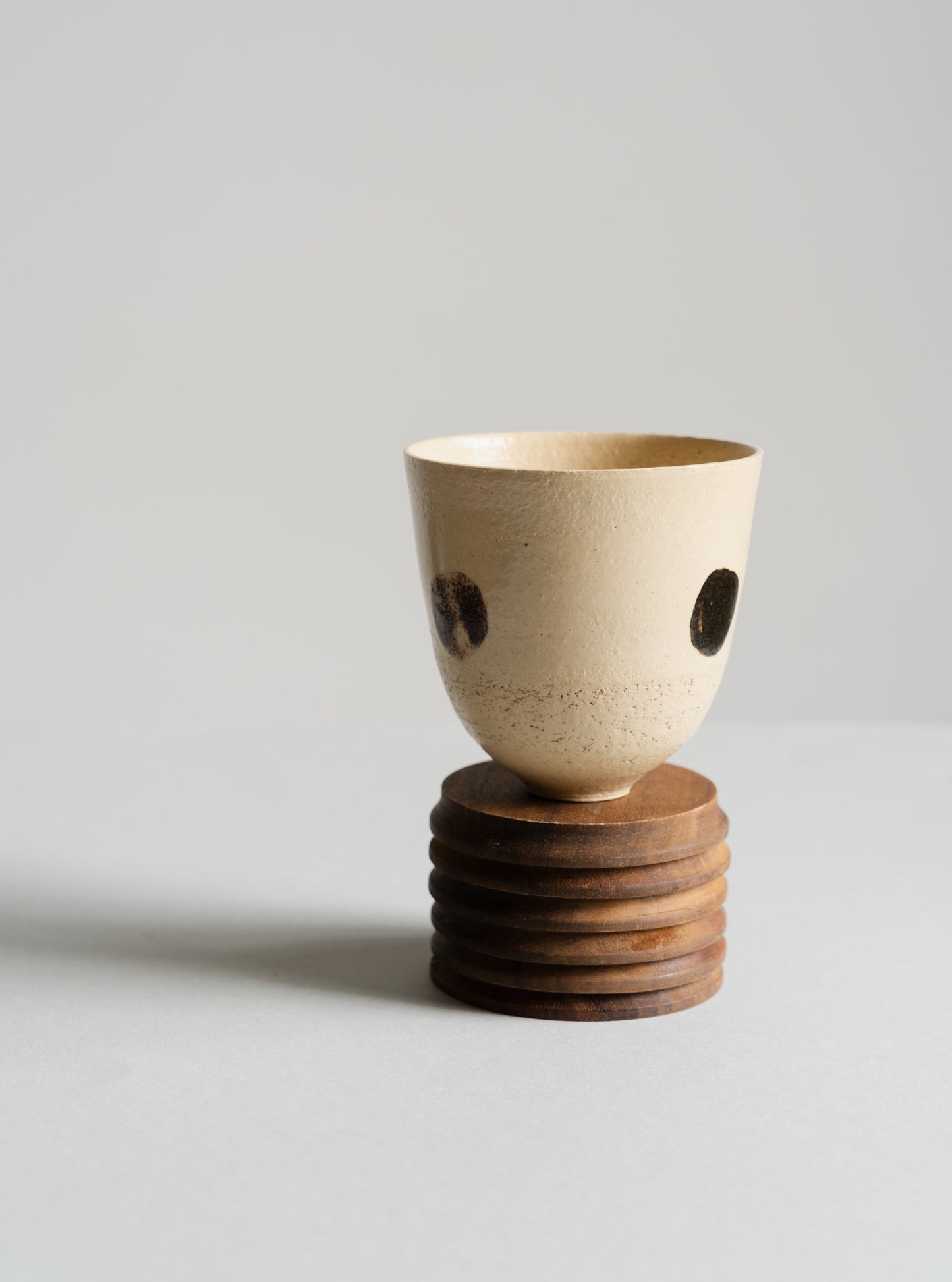 Ceramic cup on a wooden base against a light grey background