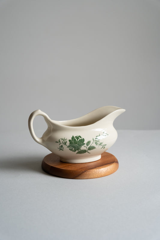 White ceramic gravy boat with green floral design on a wooden stand against a gray background