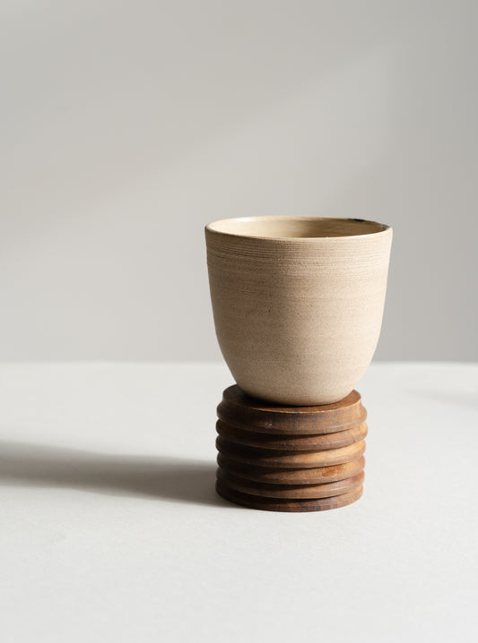 Ceramic cup on a wooden base against a plain background